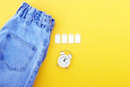 Flat lay, detail of jeans, blank white labels on yellow background.の写真素材