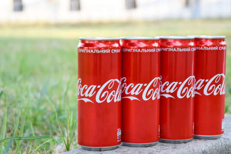 KHARKIV, UKRAINE - AUGUST 9, 2021: Many cans of Coca-Cola soda with background blurring in a park....