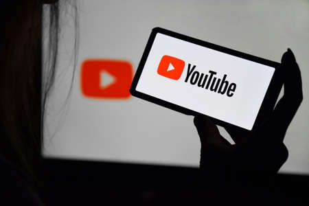 A phone with a YouTube screen in the hands of a young girl against the background of a monitor....