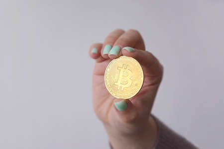 The girl holds a golden bitcoin in her hand on a light background. Digital money and bitcoin...