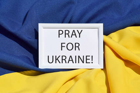 The inscription PRAY FOR UKRAINE against the background of the state flag of Ukraine, UA. Blue and yellow colors. Wat in Ukraine.の写真素材