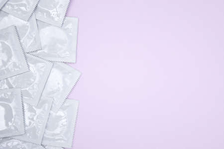 Many white packages of unopened condoms on a pink background. Using a condom to reduce the chance of...