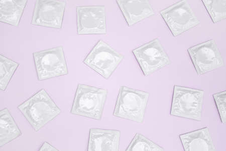 Many white packages of unopened condoms on a pink background. Using a condom to reduce the chance of pregnancy or sexually transmitted diseases, STDs. The concept of safe sex and reproductive health.の写真素材