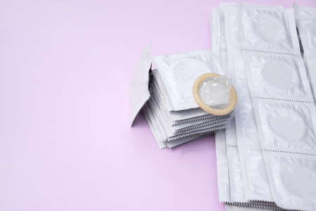 Many white packages of unopened condoms on a pink background. Using a condom to reduce the chance of pregnancy or sexually transmitted diseases, STDs. The concept of safe sex and reproductive health.の写真素材
