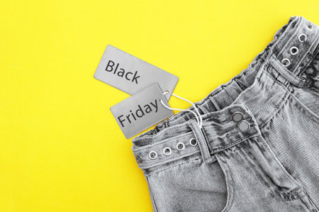 Flat lay, detail of black jeans, gray labels and inscription Black Friday on yellow background....