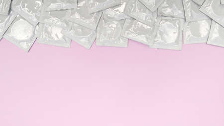 Many white packages of unopened condoms on a pink background. Using a condom to reduce the chance of...
