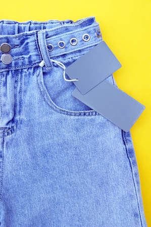 Flat lay, detail of denim jeans with blank gray label on yellow background. Shopping and discount concept. Black Friday.の写真素材