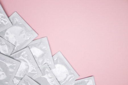 Many white packages of unopened condoms on a pink background. Using a condom to reduce the chance of pregnancy or sexually transmitted diseases, STDs. The concept of safe sex and reproductive health.の写真素材