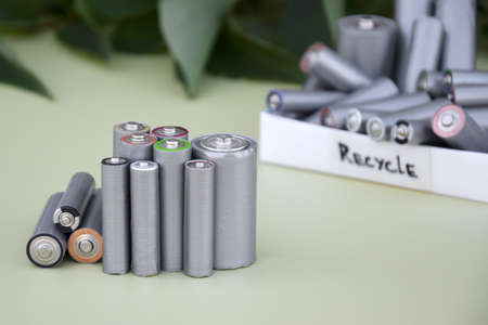 Used AA batteries and proper disposal of environmentally and soil-toxic batteries on a green background.の写真素材