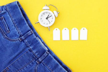 Flat lay, detail of jeans, blank white labels on yellow background.の写真素材