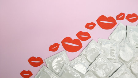 Many white packages of unopened condoms with paper kisses on a pink background. Using a condom to reduce the chance of pregnancy or sexually transmitted diseases, STDs. The concept of safe sex and reproductive health.の写真素材