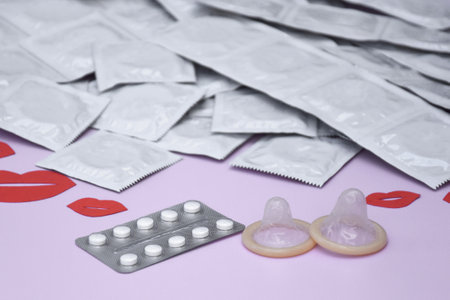 Many white packages of unopened condoms with paper kisses. Using a condom to reduce the chance of...