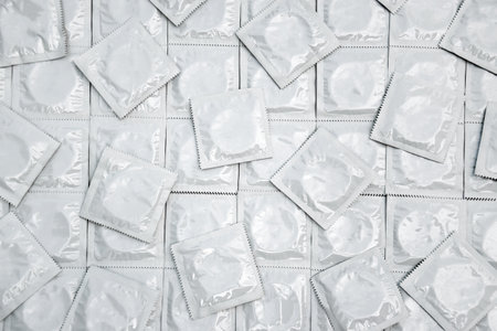 Many white packages of unopened condoms as a background. Using a condom to reduce the chance of...