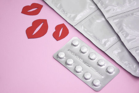 Many white packages of unopened condoms with paper kisses. Using a condom to reduce the chance of...