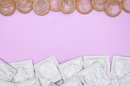 Many white packages of unopened condoms on a pink background. Using a condom to reduce the chance of pregnancy or sexually transmitted diseases, STDs. The concept of safe sex and reproductive health.の写真素材