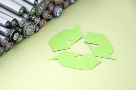 Used AA batteries and proper disposal of environmentally and soil-toxic batteries on a green background. The concept of processing harmful and recyclable objects.の写真素材