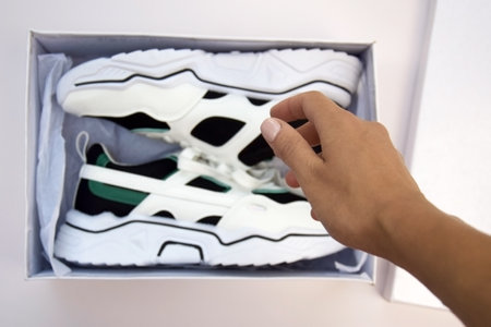 Bright female sneakers in white box on light pink background. Fashion blog or magazine concept....