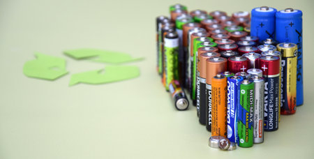 Used AA batteries and proper disposal of environmentally and soil toxic batteries on a green background.のeditorial素材