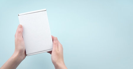 Female hands holding white package box on blue background. Packaging, shopping, delivery concept.