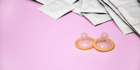 Many white packages of unopened condoms on a pink background. The concept of safe sex and...