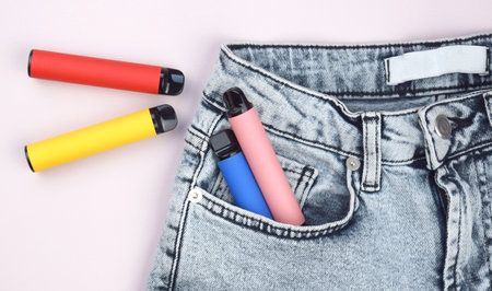 A set of multi-color disposable electronic cigarettes in a jeans pocket. The concept of modern smoking, vaping and nicotine.の写真素材