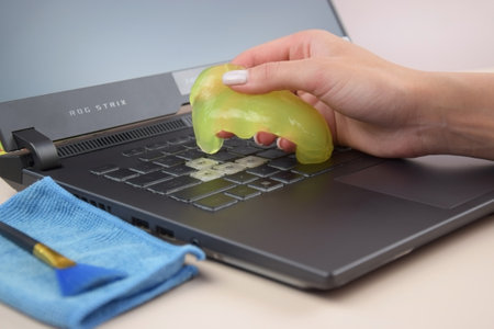 Kharkiv, Ukraine, JULY 11, 2023: Green soft cleaning gel for cleaning dust on a laptop keyboard Asus Rog Strix. The concept of cleaning your computer keyboard. Office cleaning.のeditorial素材