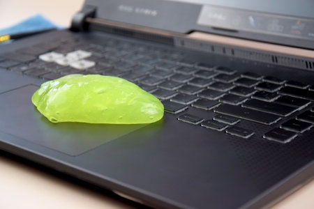 Kharkiv, Ukraine, JULY 11, 2023: Green soft cleaning gel for cleaning dust on a laptop keyboard Asus Rog Strix. The concept of cleaning your computer keyboard. Office cleaning.のeditorial素材