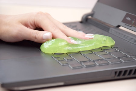 Kharkiv, Ukraine, JULY 11, 2023: Green soft cleaning gel for cleaning dust on a laptop keyboard Asus Rog Strix. The concept of cleaning your computer keyboard. Office cleaning.のeditorial素材
