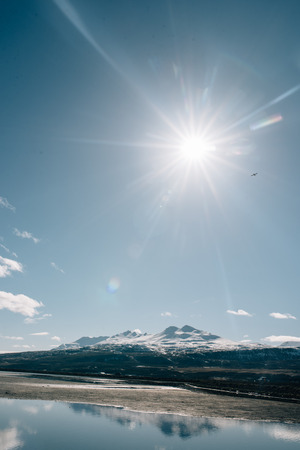 Lake mountains in Iceland plane in the sky water stones sun snowの写真素材