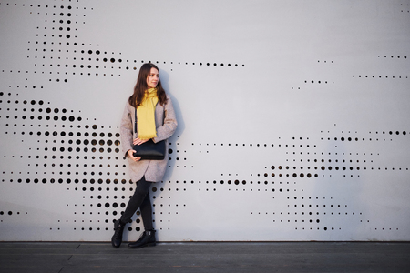 girl with a scarf with a black bag in a coat against the wallの写真素材