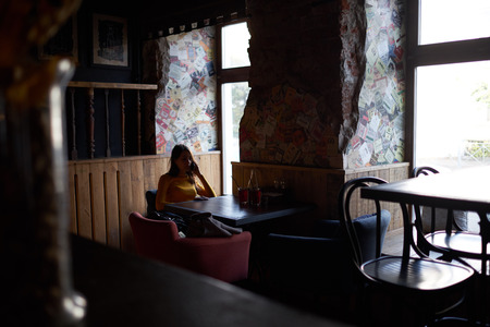girl sitting at a table in a restaurant and talking on the phoneの写真素材