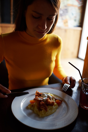 girl eat chicken in breading with mashed potatoes on a dish fork and knifeの写真素材