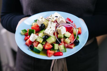 greek salad on a blue plate in the hands of a waitressの写真素材