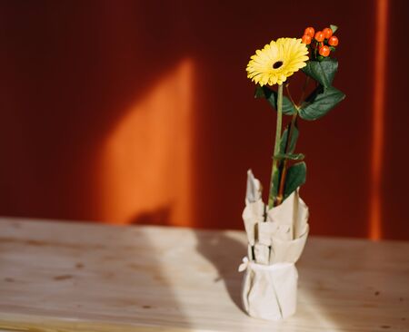 yellow gerbera flower in a craft vase on a table backlit by the sunの写真素材