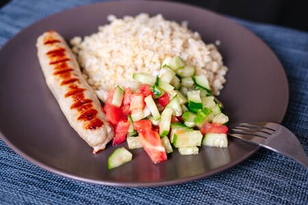 dinner on a plate with pork sausage bulgur and tomato and cucumber salad. Close-upの写真素材
