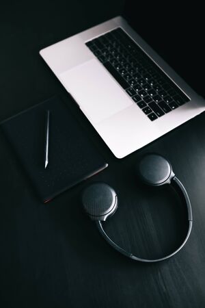 Dark modern workplace with a graphic tablet, laptop, wireless headphones