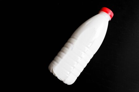 Transparent plastic bottle for milk with a red cap on a black backgroundの写真素材