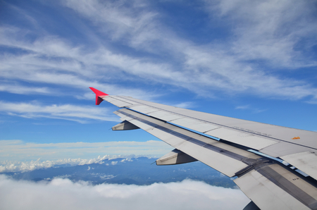 Wing of an airplane flying above the clouds. people looks at the sky from the window of the plane, using air transport to travel or go homeの写真素材