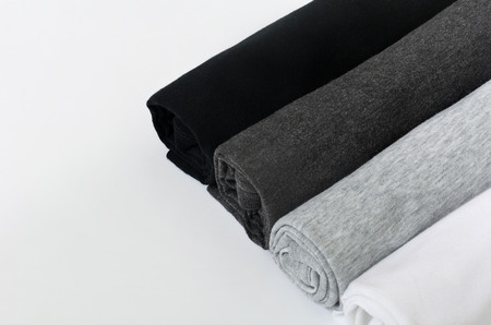 stack of black, grey and white (monochrome) t-shirt rolled up on white background, copy spaceの写真素材