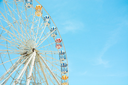 front view of half retro colorful ferris wheel at amusement park over blue sky background, copy space, vintage effectのeditorial素材