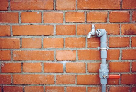 outdoor faucet water tap with gray PVC pipe and red valve   on red brick wall background texture,...