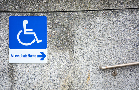 wheelchair ramp sign for the disabled on  dirty pebbles stone wall texture with steel railing in public place, copy spaceの写真素材