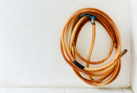 water tap with rolled of old leak rubber tube on white cement wall background, copy spaceの写真素材