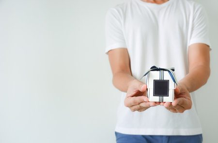 male hands holding a small white gift box wrapped with blue and silver color ribbon and dark blue blank label on white background, copy spaceの写真素材