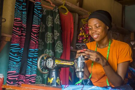 young african woman who is a tailor smiling while using her mobile phoneの写真素材