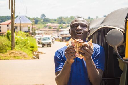 cheerful african man winner holding some money celebrating and jubilant standing next to an auto rickshaw taxi outdoorの写真素材