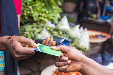 close up of an african woman selling in a local african market holding a mobile point of sale device collecting a credit card from a customerの写真素材