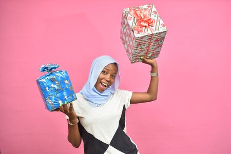 beautiful young black lady holding gift boxes and presents smiling and feeling excited, in front of...