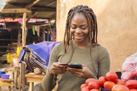 young african woman selling in a local african market using her mobile phone and credit card to do a transaction online smilingの写真素材