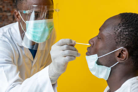 an african medical personnel taking nasal sample for covid-19 testingの写真素材